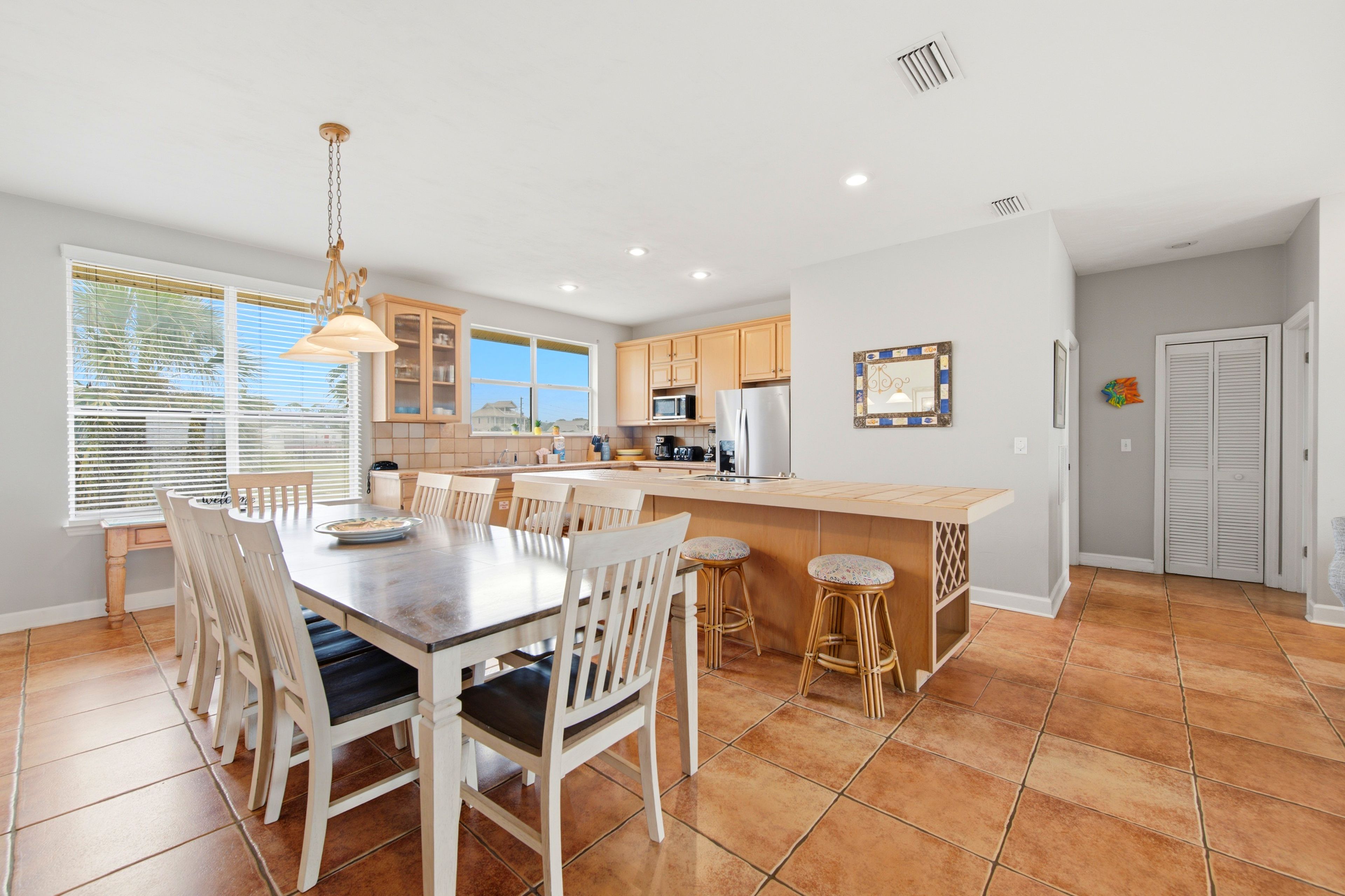 A modern kitchen with a dining area, featuring a large island, wooden cabinets, and a view to the outside.