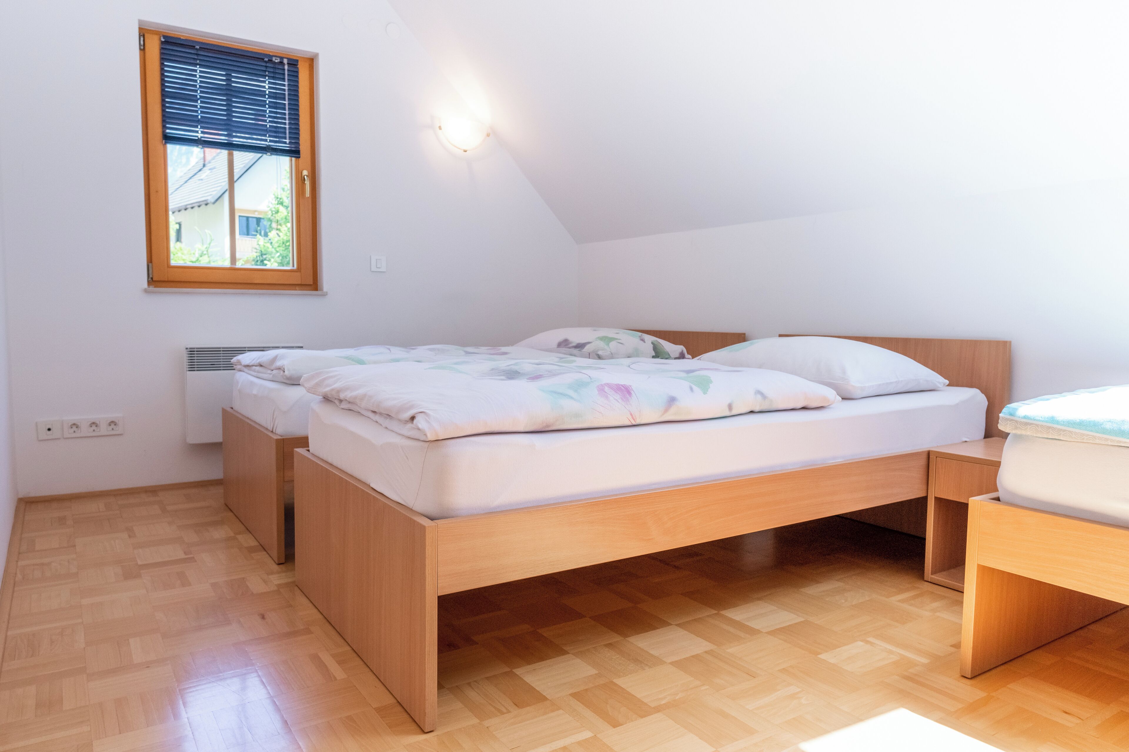 A bedroom with a wooden bed, a window with blinds, and a wall-mounted light fixture.