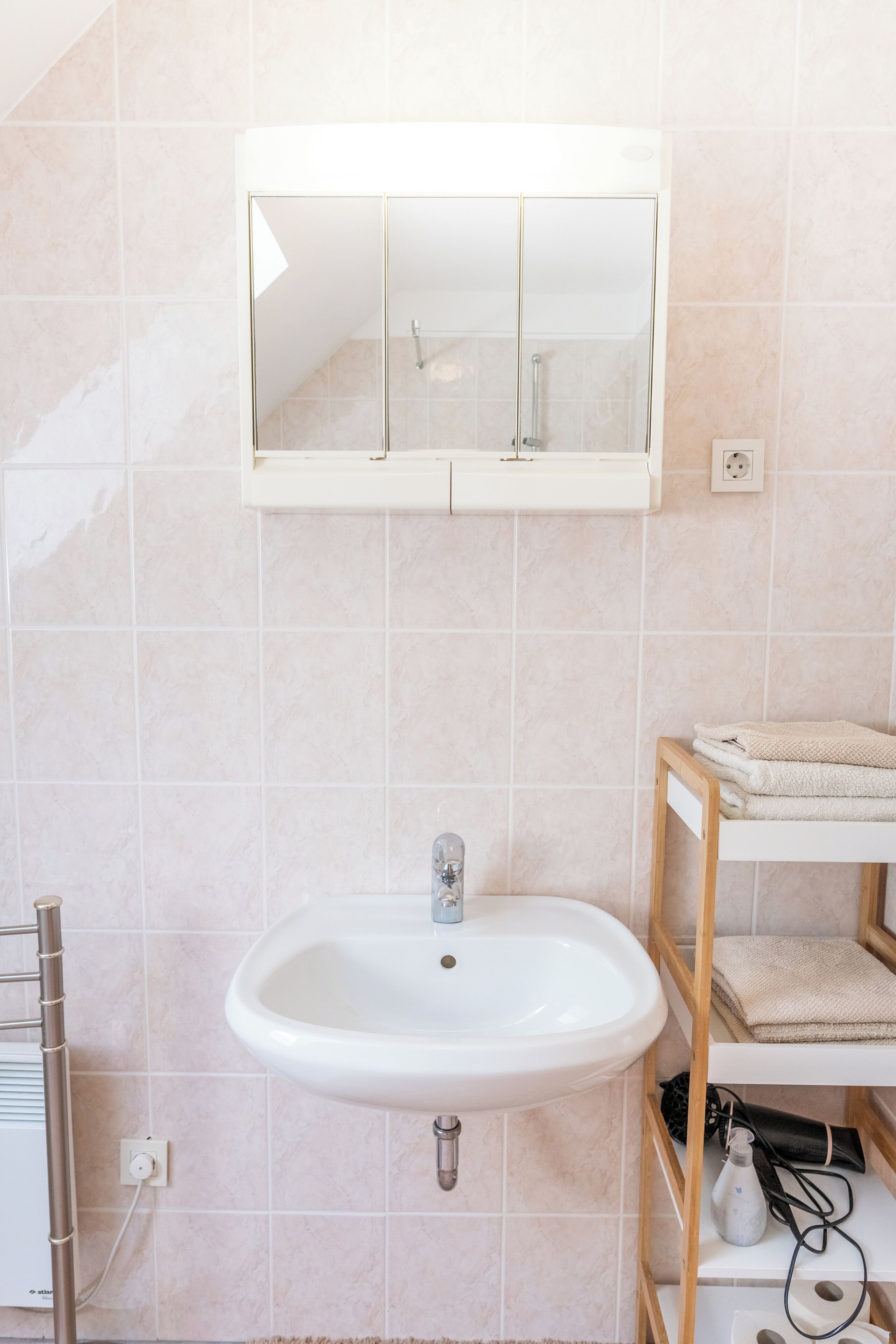 A bathroom with a white sink, a mirror above it, and a towel rack to the left.