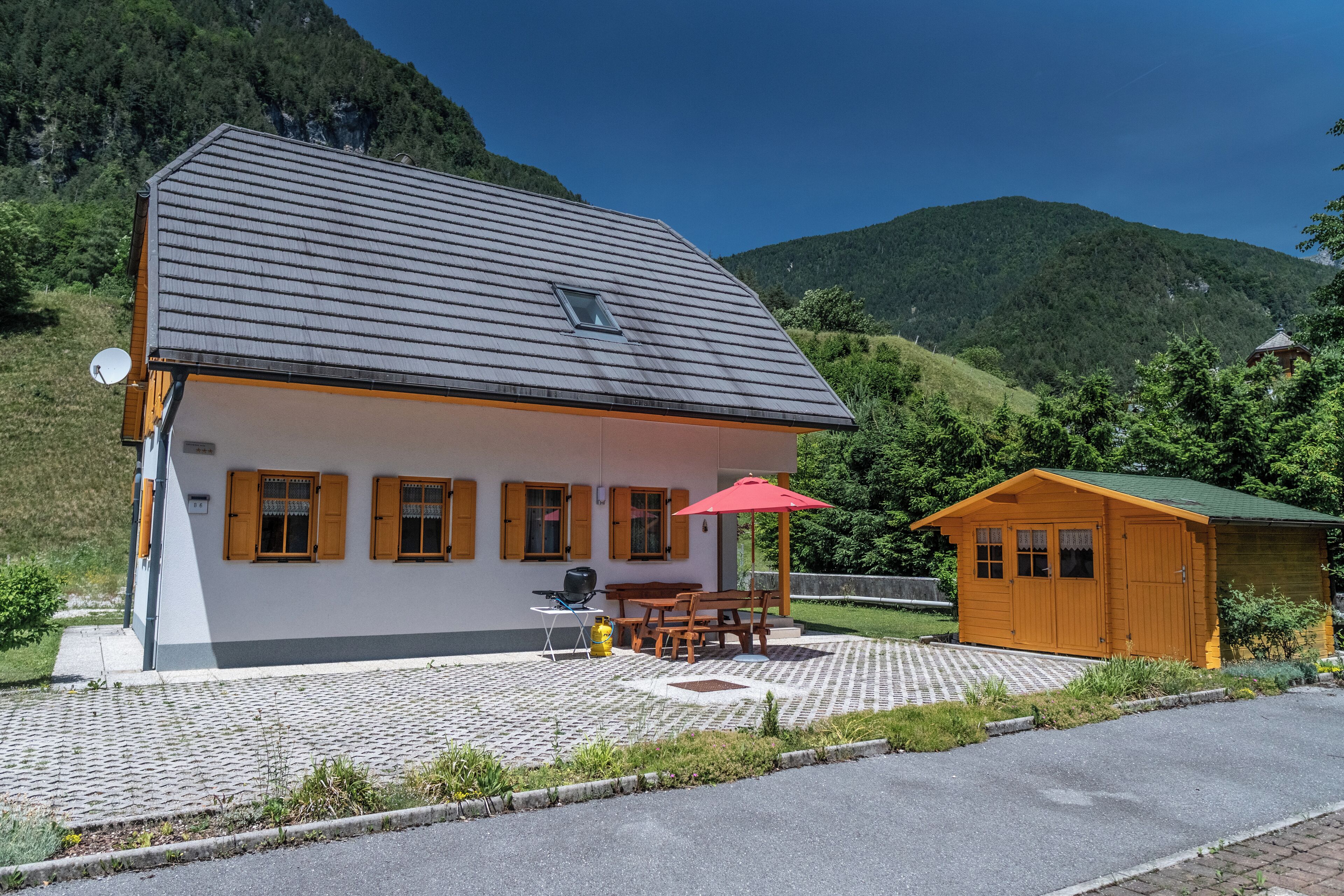 A two-story building with a sloped roof, a satellite dish, and a red umbrella.