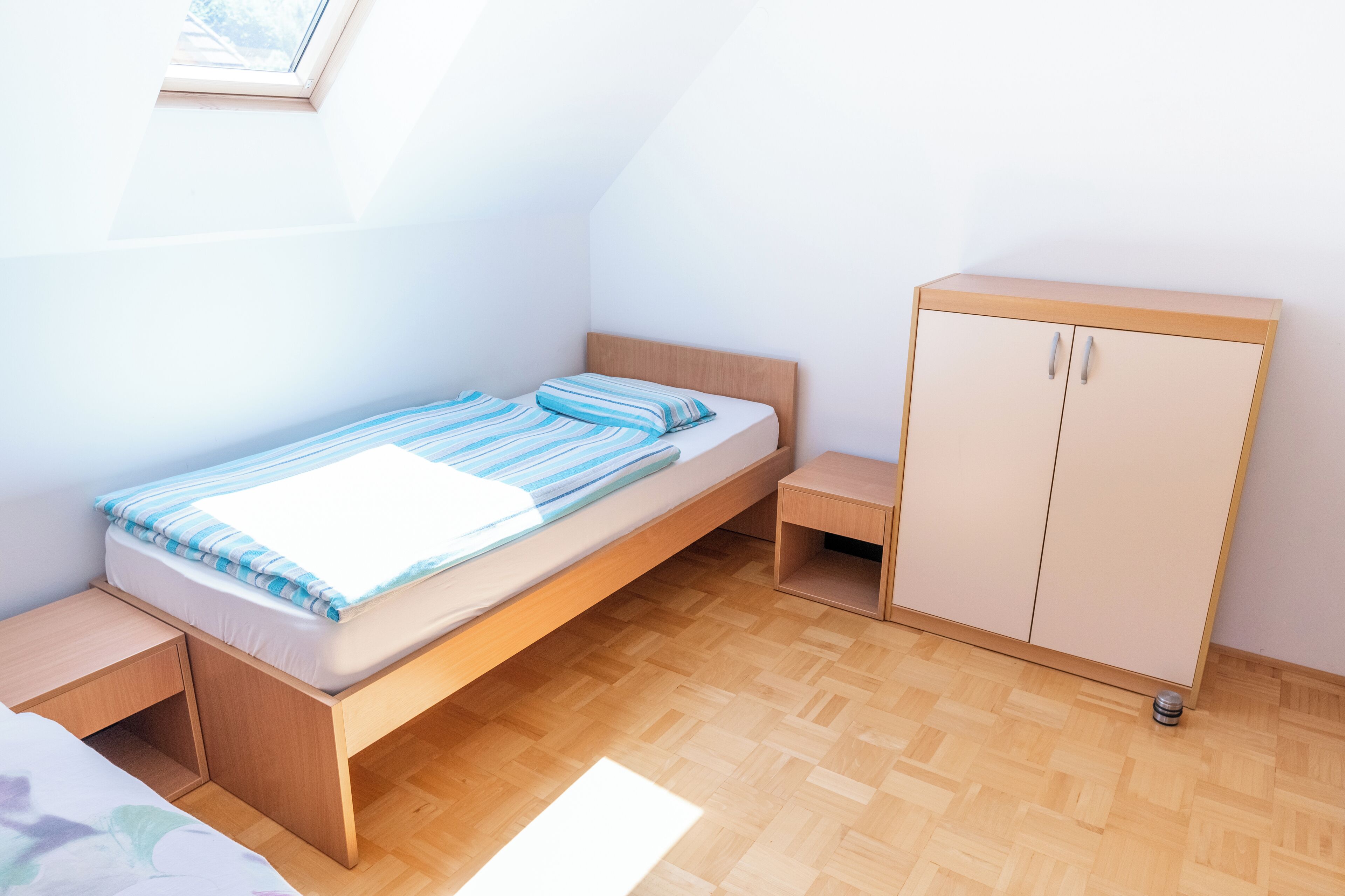 A small, single-bed room with a wooden headboard and a wooden wardrobe.