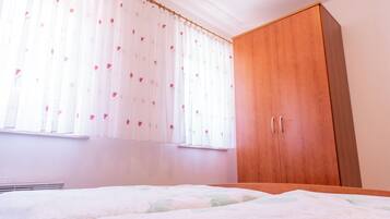 A bedroom with a wooden wardrobe, a bed with a floral bedspread, and sheer curtains with a heart pattern.