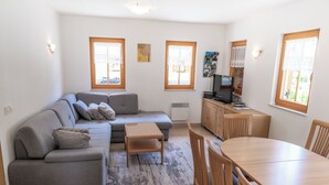 A modern living room with a grey sofa, a wooden dining table, and a TV. - House Parabola – 4-Bedroom Mountain Retreat with Breathtaking Views, Sleeps 10 (Log pod Mangartom)