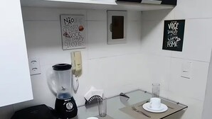 A compact kitchen with a glass dining table, two chairs, a black blender, and a small potted plant on the shelf.