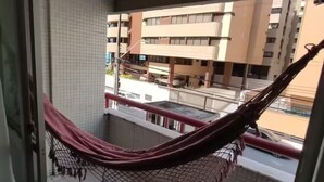 A balcony with a hammock, tiled floor, and a view of a multi-story building.