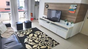 A modern living room with a sofa, a flat-screen TV, a patterned rug, and a balcony with a view of the street.