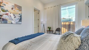 Et soveværelse med en seng, et billede, en lampe og udsigt ud.