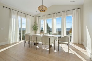 A spacious dining area with a high ceiling, large windows, and a view of the outdoors. - Ultimate Multi-Family & Reunion Retreat (Heber City)