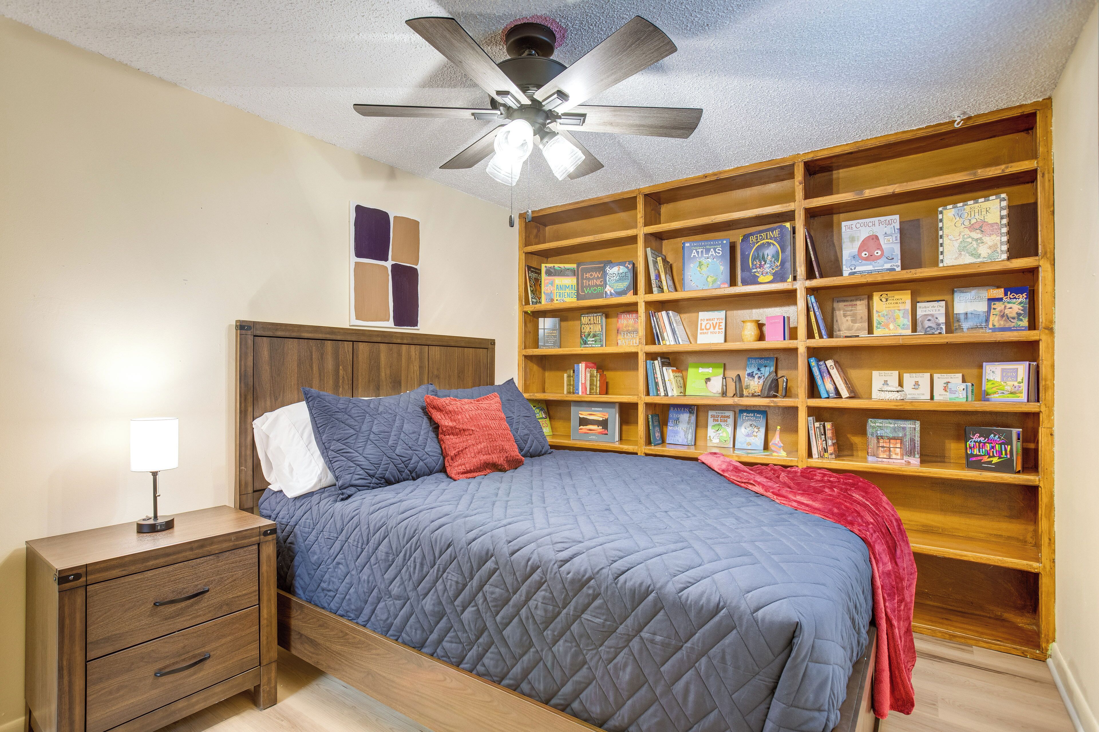 A bedroom with a bed, a nightstand, a bookshelf, and a ceiling fan.