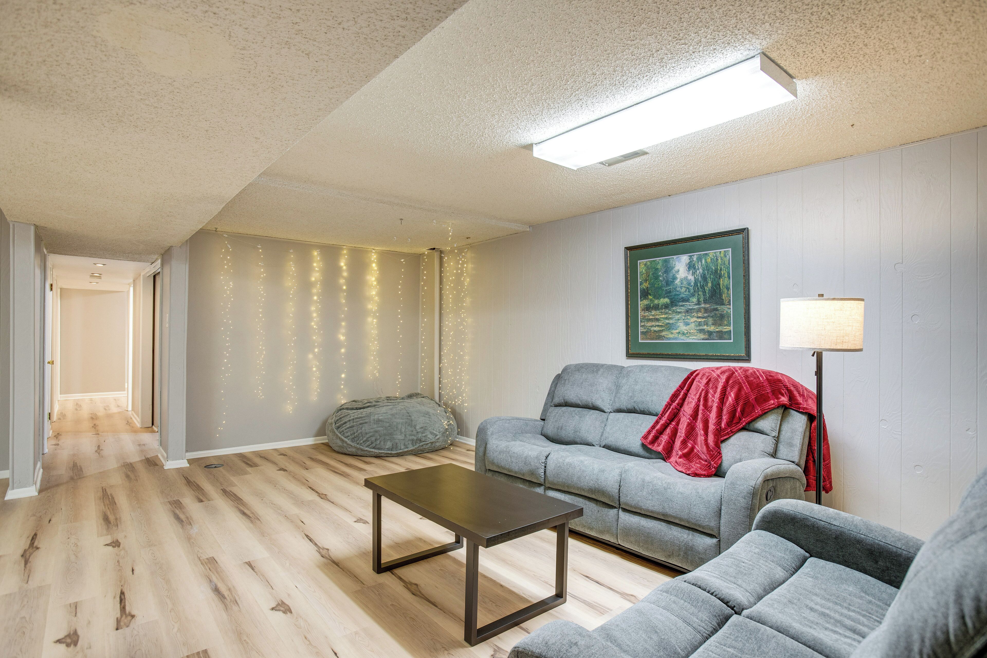Un salon avec un canapé gris, une petite table et un fauteuil en forme de poire. Il y a un tableau au mur et une lampe à côté du canapé.