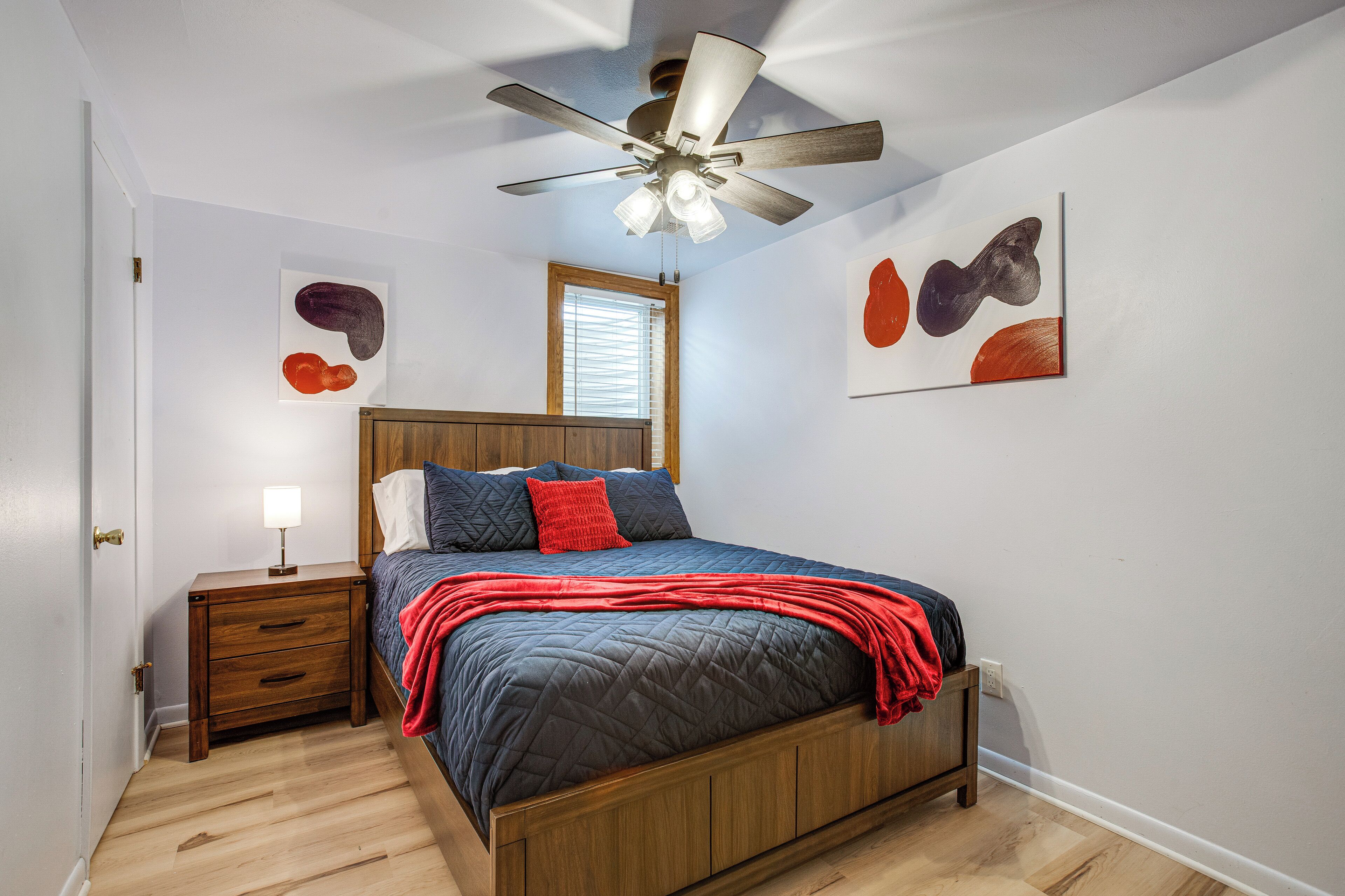 A bedroom with a wooden bed, a nightstand, a ceiling fan, and artwork on the walls.