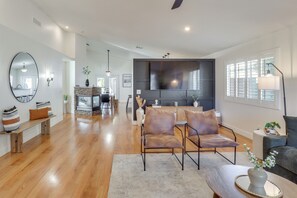 A spacious living room with a wooden floor, a large mirror, a sofa, and a dining area with a stone fireplace. - Extended Stay Home w/ Mtn View: 5 Mi to The Strip! (Las Vegas)