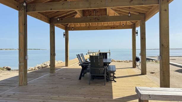 Une terrasse en bois avec une table et des chaises, donnant sur une étendue d’eau calme.