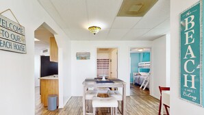 Une pièce chaleureuse avec une table et un banc en bois, une télévision et une pancarte sur laquelle on peut lire : « BIENVENUE DANS NOTRE MAISON DE VACANCES EN BORD DE MER ».