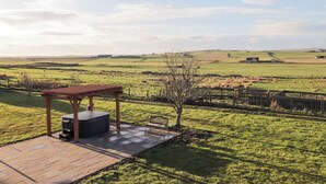 A patio with a wooden pergola and a seating area overlooking a rural landscape with fields and distant buildings. - Northbanks House (Thurso)
