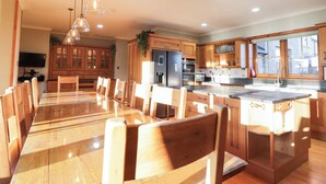 A spacious kitchen with wooden cabinets, a large dining table, and pendant lighting. - Northbanks House (Thurso)