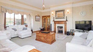 A spacious living room with a fireplace, a television, and a large window with curtains. - Northbanks House (Thurso)