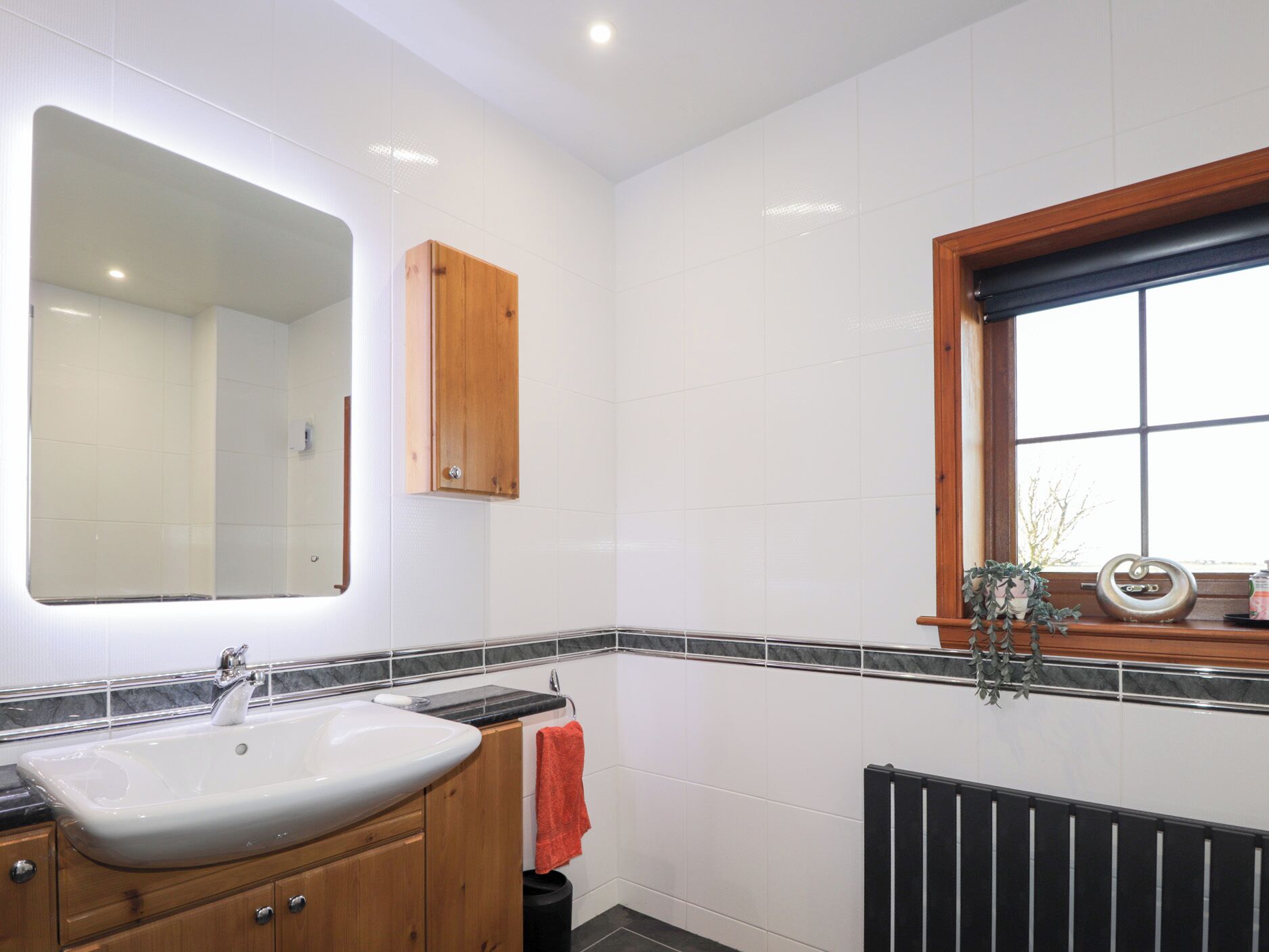 Un baño con lavamanos blanco, armarios de madera, un espejo y una ventana con vistas.
