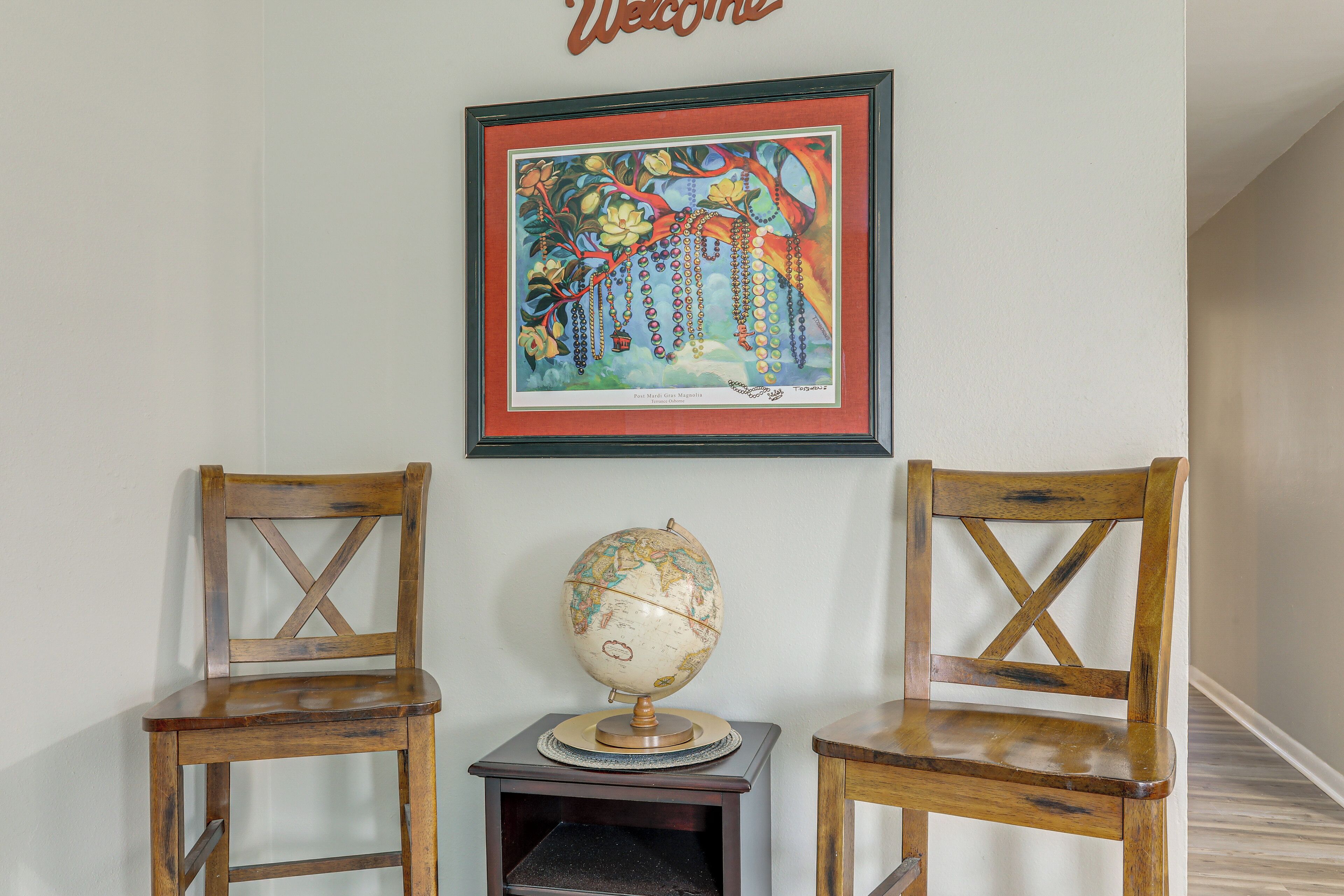 A framed welcome sign above two wooden chairs with a globe on a small table between them.