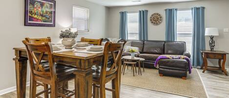 A dining area with a wooden table and chairs, a sofa, and a rug.