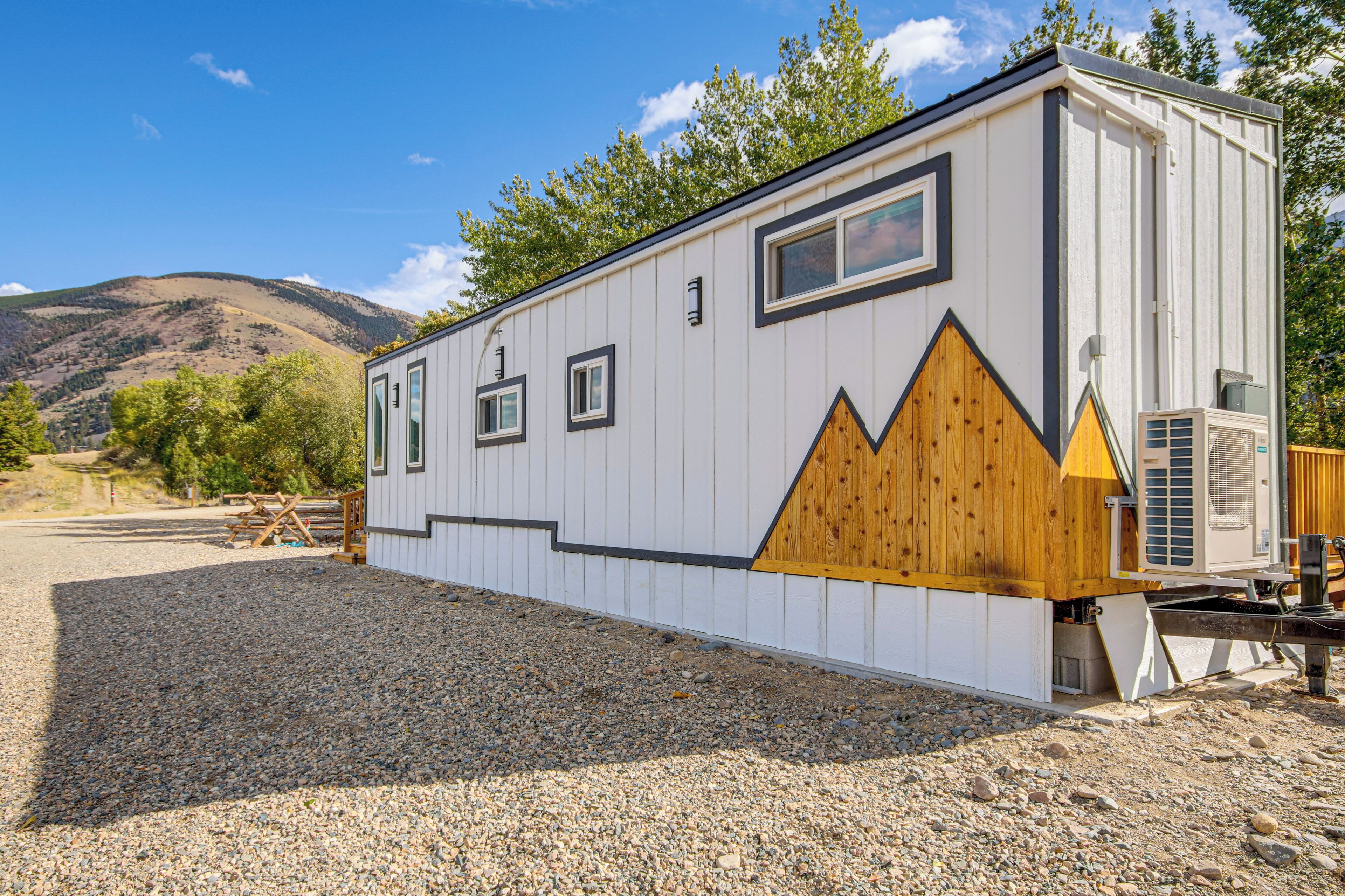 A single-story RV with a white exterior and a wooden accent wall, located in a gravel area with a mountain backdrop.