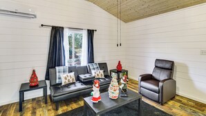 Ein Wohnzimmer mit einem schwarzen Ledersofa, einem braunen Ledersessel, einem Couchtisch mit Weihnachtsdekoration und einem Fenster mit Vorhängen.
