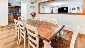 Un comedor con una mesa y sillas de madera, una araña y un espejo grande en la pared.