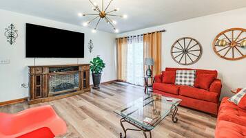 A living room with a flat-screen TV, a fireplace, a red sofa, a glass coffee table, and decorative wheels on the wall.