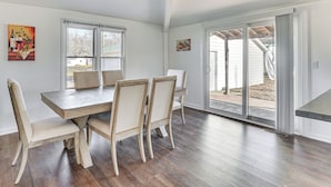 Een eetgedeelte met een houten tafel en stoelen, grote ramen en uitzicht op buiten.