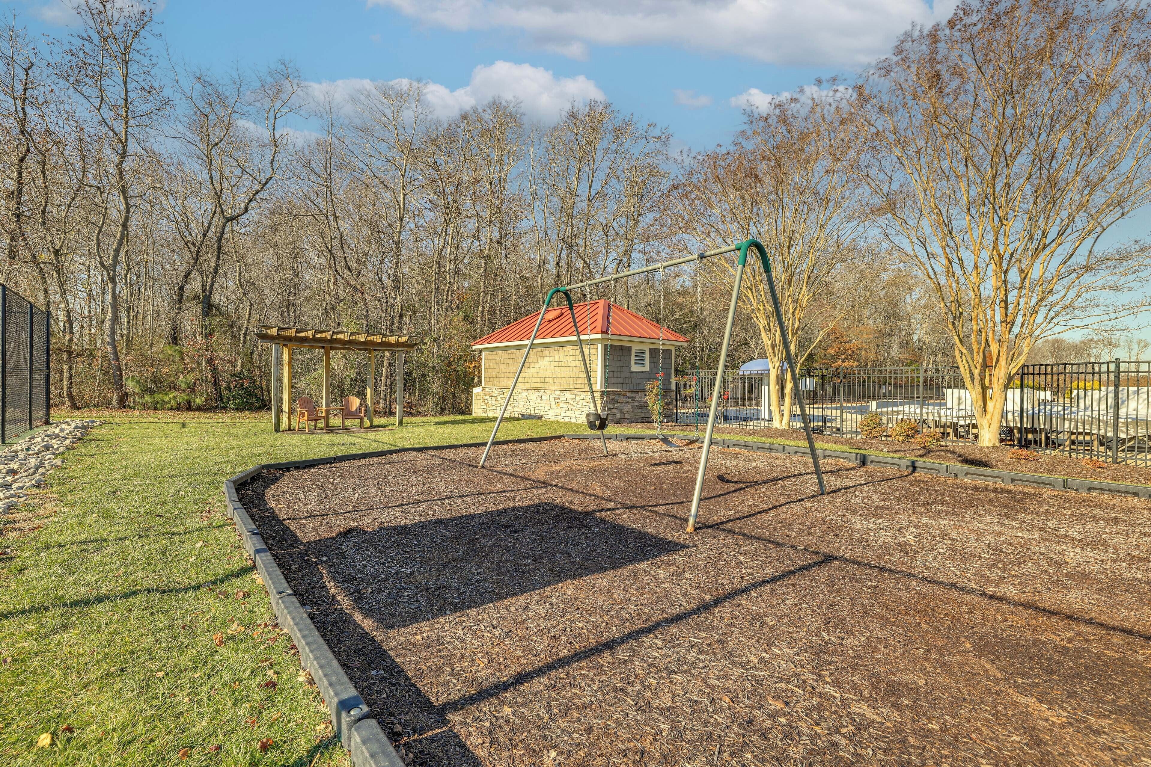 A playground with a swing set, a small shed, and a fenced area with trees.