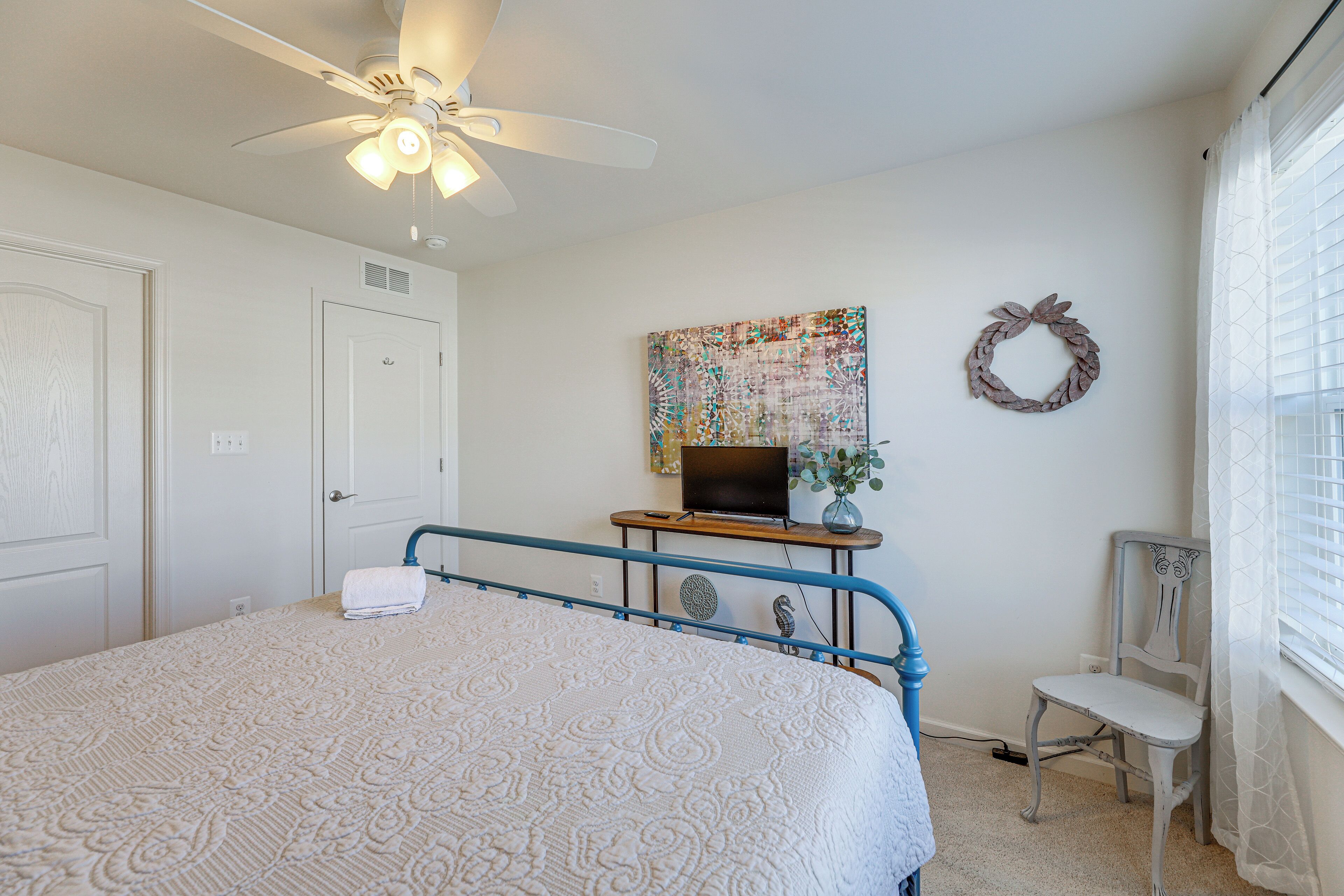 A bedroom with a bed, a ceiling fan, a desk with a computer, a chair, and a wall decoration.