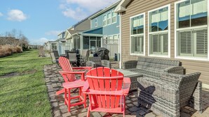 A patio area with outdoor furniture, including red Adirondack chairs and wicker sofas, adjacent to a building with large windows and a covered patio. - Shuttle to Beach, Relax on Patio! Millville Escape (Millville)