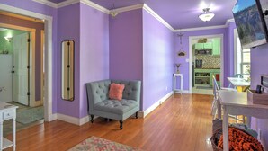 A room with purple walls, a grey upholstered armchair, a white table, and a wooden floor.