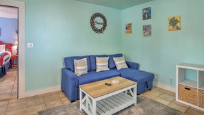 A living room with a blue sofa, a wooden coffee table, and a white side table. There are wall decorations and a door leading to another room. - New Listing! Rosewood Studio at Dusty Rose Inn | Main Street Creede (Creede)