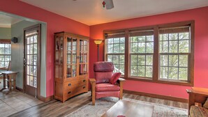 A room with a wooden cabinet, a red leather chair, a table, and large windows with a view of trees. - New Listing! Roseview Loft at Dusty Rose Inn | Main Street Creede | (Creede)