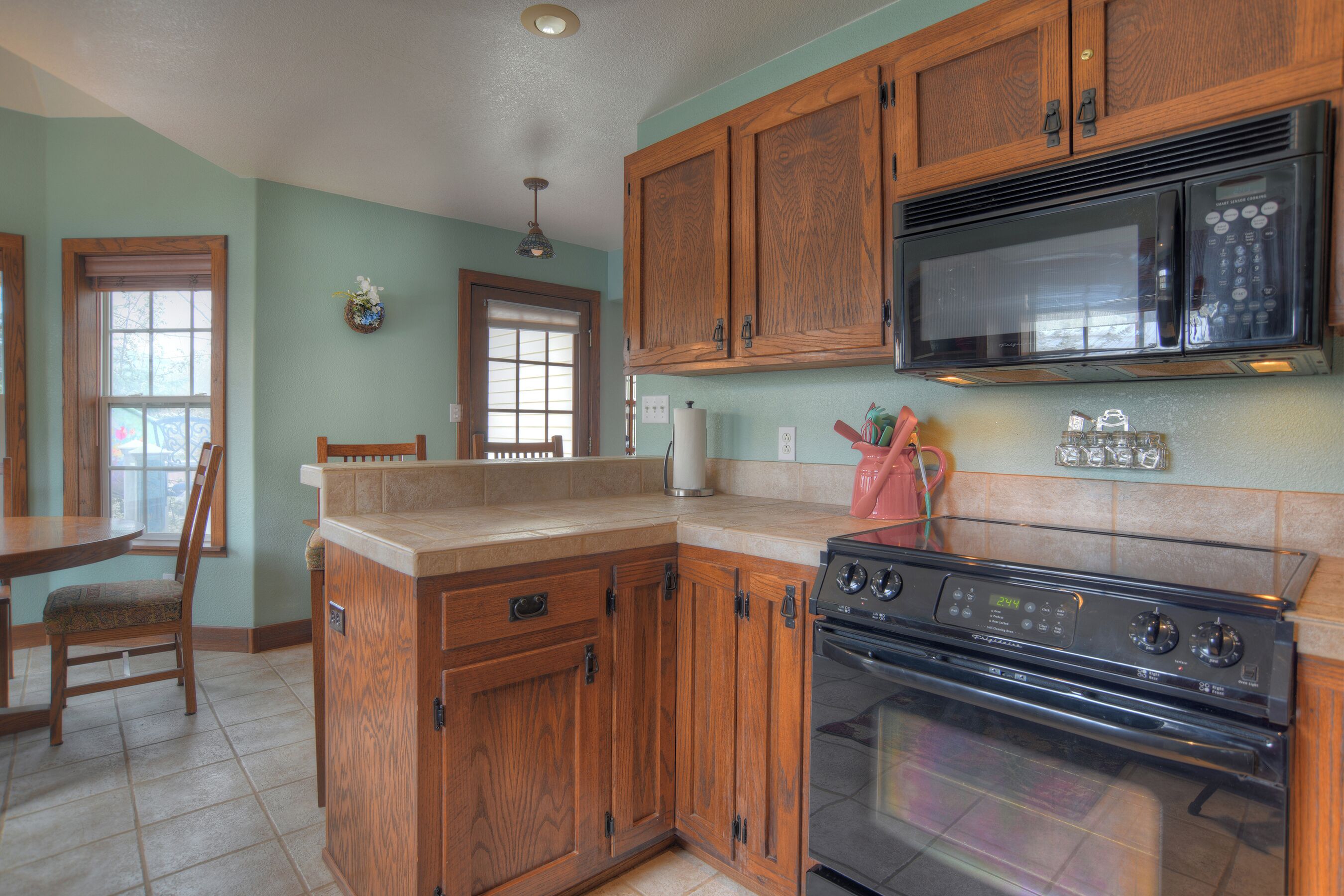 A kitchen with wooden cabinets, a microwave, an oven, and a dining area with a chair and table.