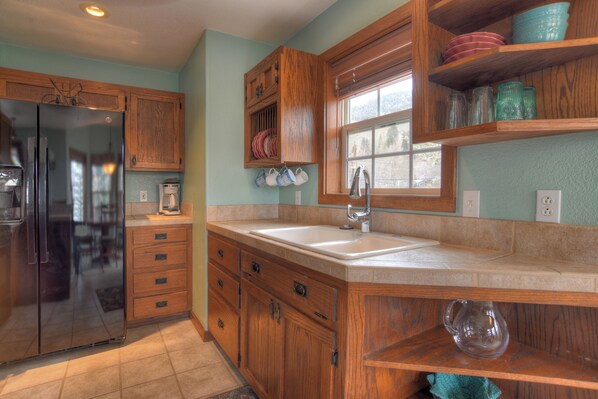A kitchen with wooden cabinets, a stainless steel refrigerator, a window, and a sink.
