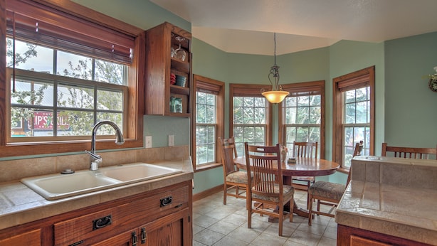 A kitchen with a sink, wooden cabinets, a dining table with chairs, and a window with a view of trees. - New Listing! Roseview Loft at Dusty Rose Inn | Main Street Creede | (Creede)