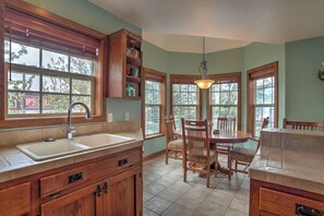 A kitchen with a sink, wooden cabinets, a dining table with chairs, and a window with a view of trees.