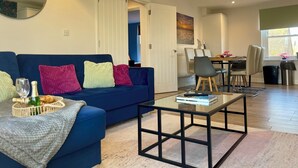 Un salon moderne avec un canapé bleu, une table basse en verre et un coin repas comprenant des chaises et une table.