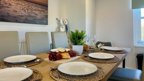 Un coin repas avec une table dressée pour quatre personnes, comprenant des assiettes, des couverts et une pièce maîtresse décorative agrémentée de pain et de raisins.