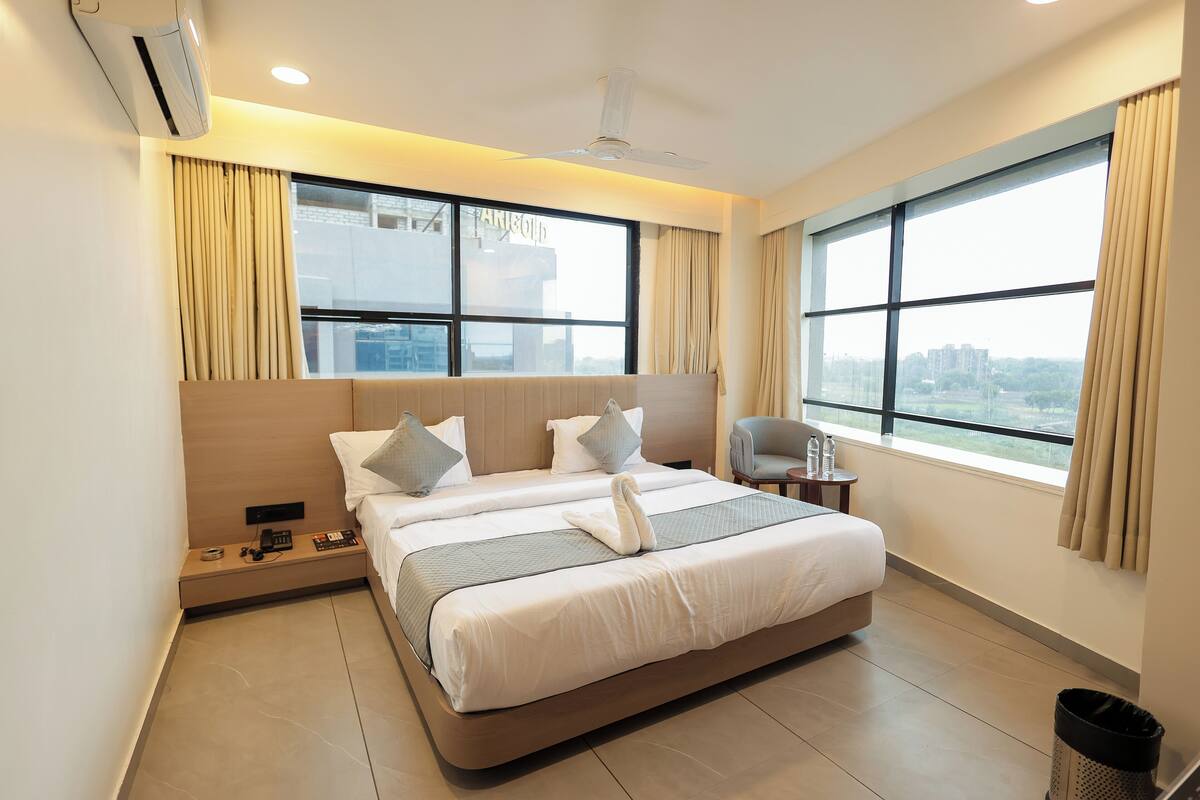 Una habitación de hotel moderna con una cama grande, dos mesitas de noche, una silla y vistas a la ciudad.