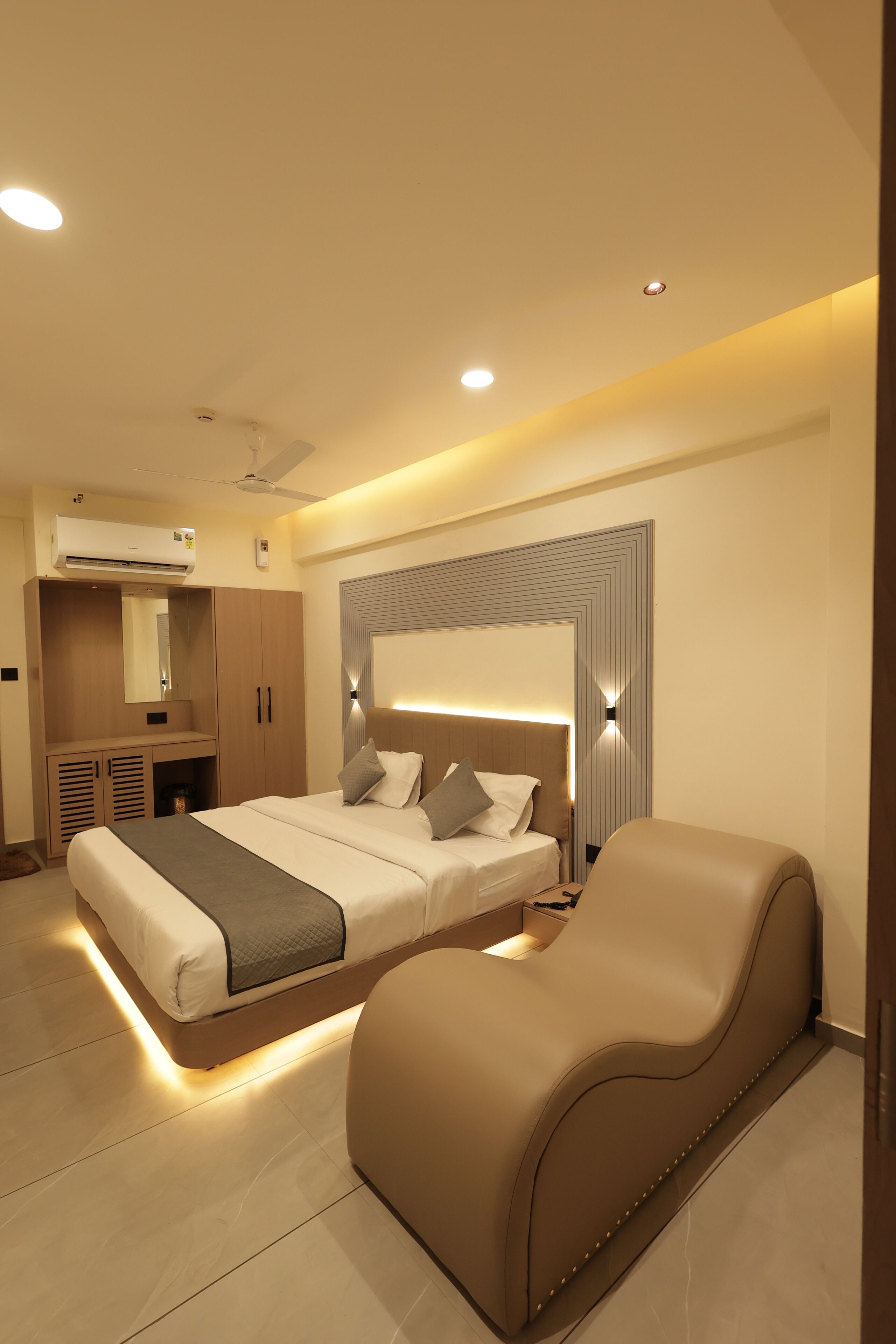 A modern bedroom with a large bed, bedside tables, a built-in wardrobe, and a seating area.
