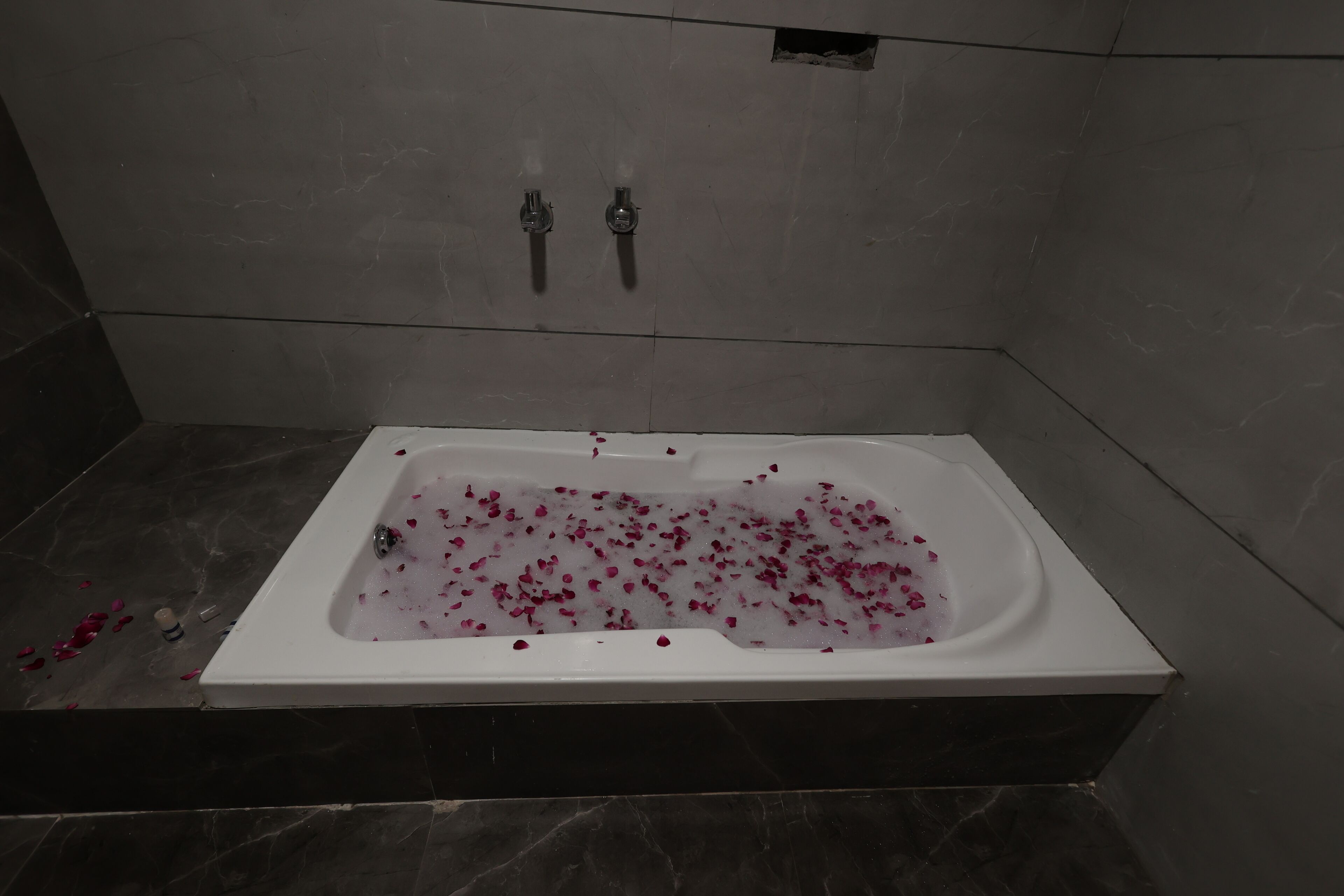 Une salle de bain moderne avec une baignoire remplie de pétales de rose, des murs en marbre et un espace douche.