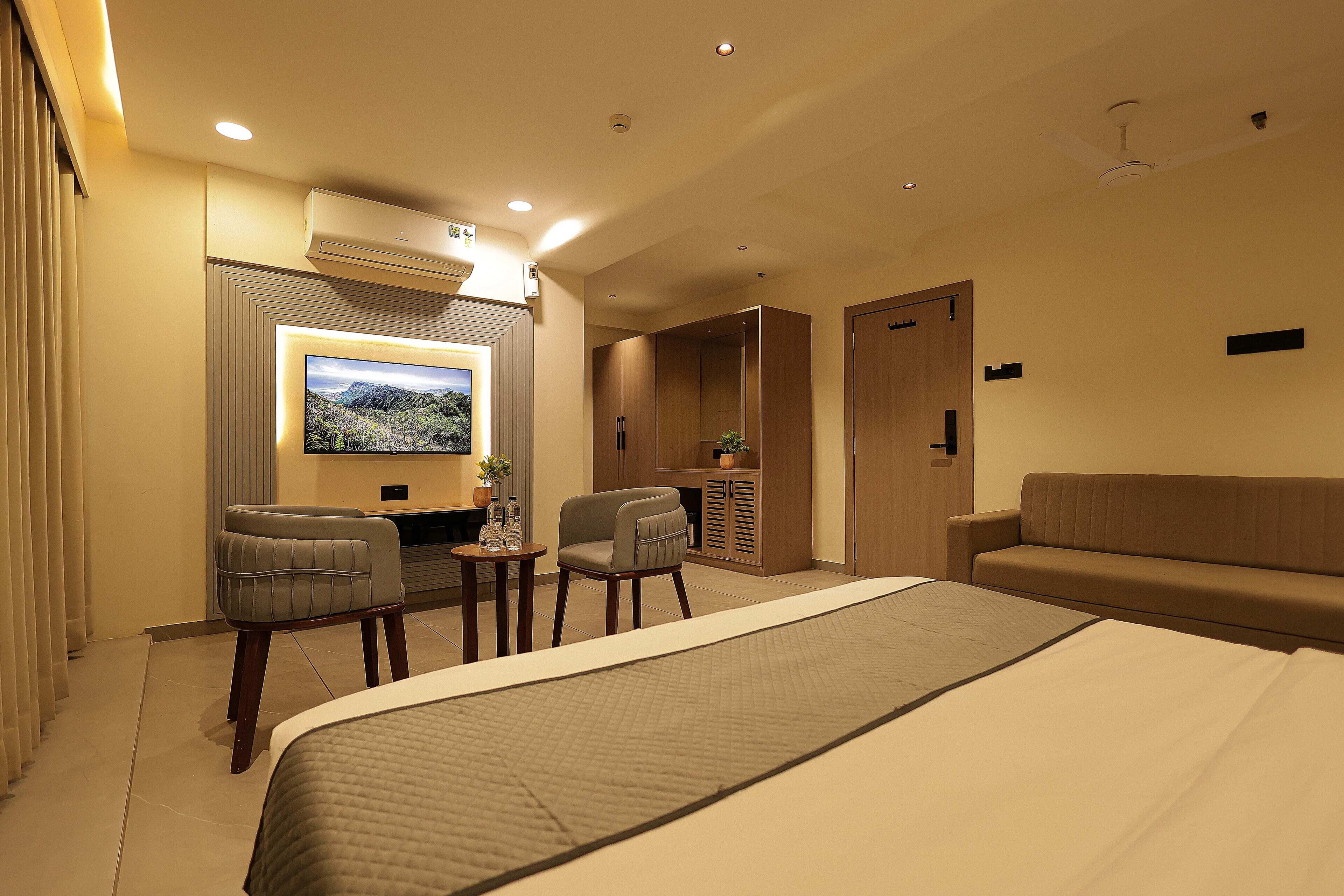 Una habitación de hotel con una cama grande, un televisor montado en la pared, una zona de estar con sillas y un armario.