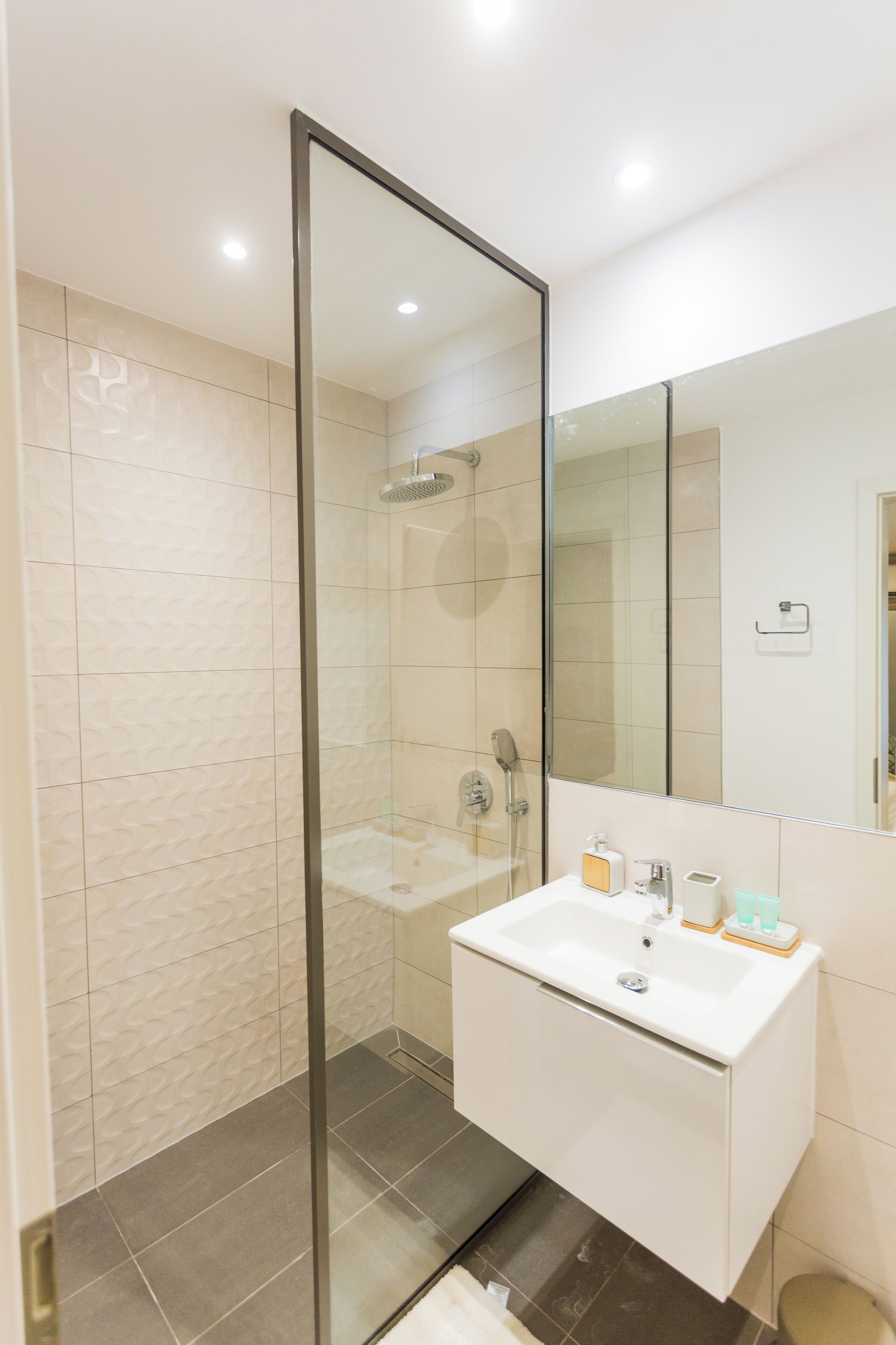 A modern bathroom with a glass-enclosed shower, a white sink, and a large mirror.