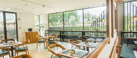 Un restaurant avec des meubles en bois, de grandes fenêtres et des luminaires suspendus.
