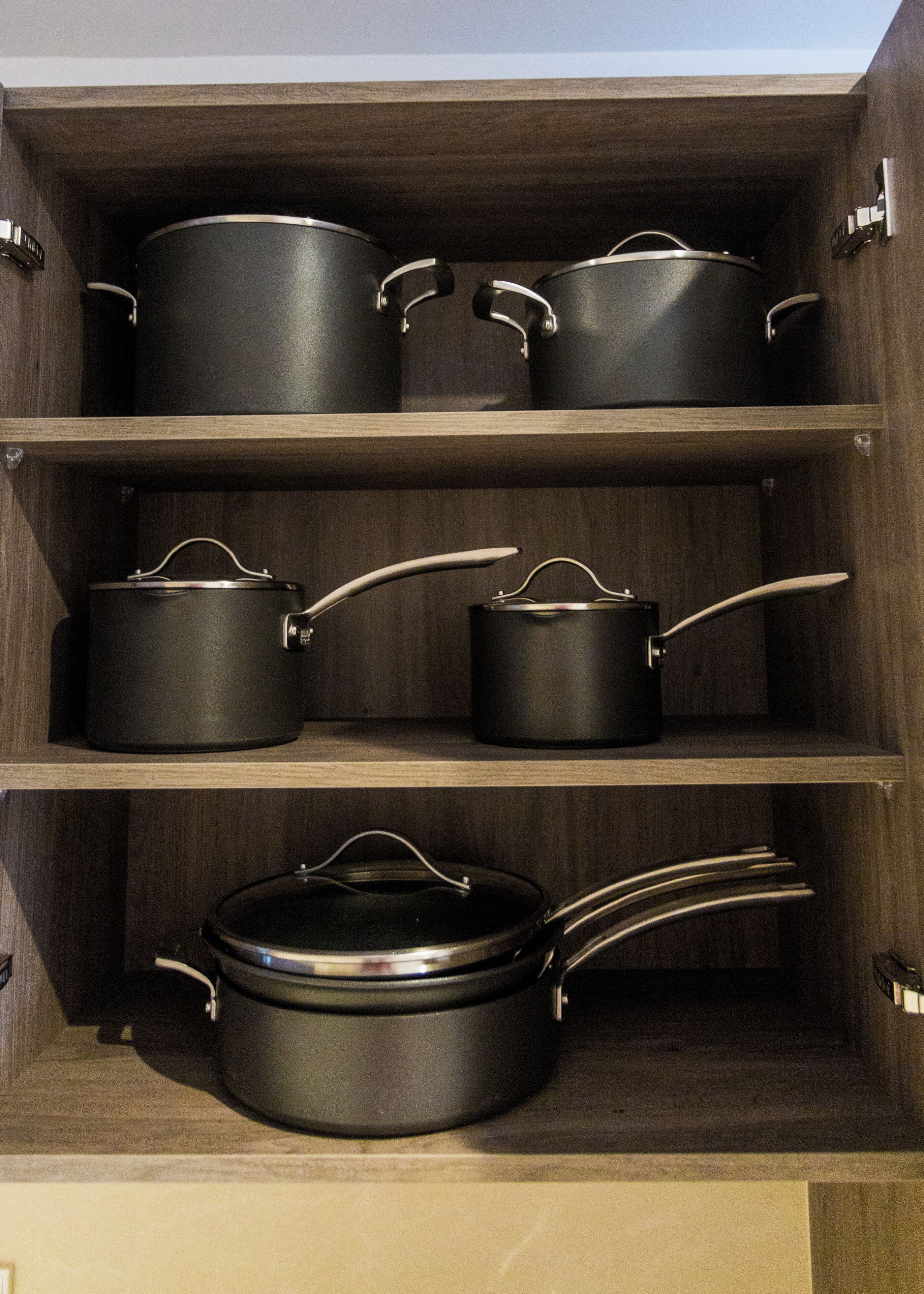 A kitchen cabinet with multiple black pots and pans.