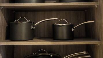 A kitchen cabinet with multiple black pots and pans.