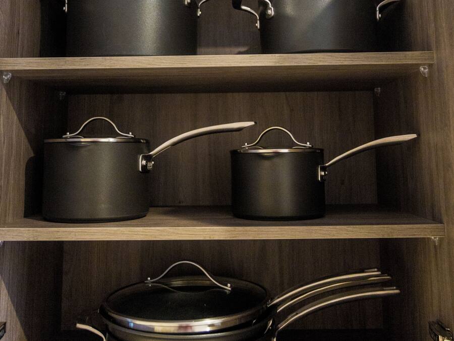 A kitchen cabinet with multiple black pots and pans.